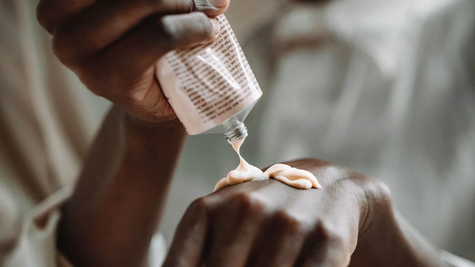 Hands applying moisturizer from a tube.