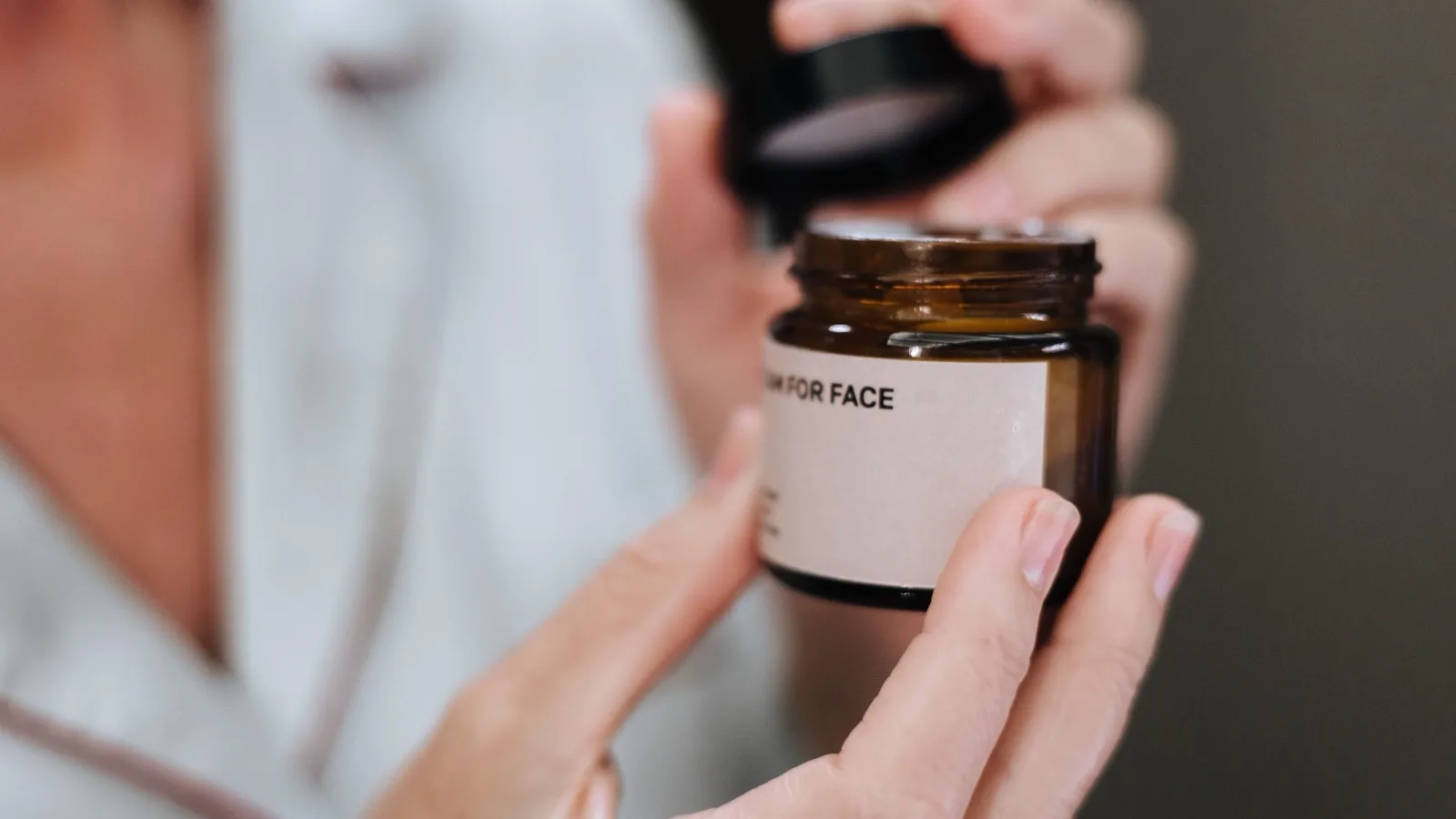 Hands opening a face cream jar as part of a skincare routine.