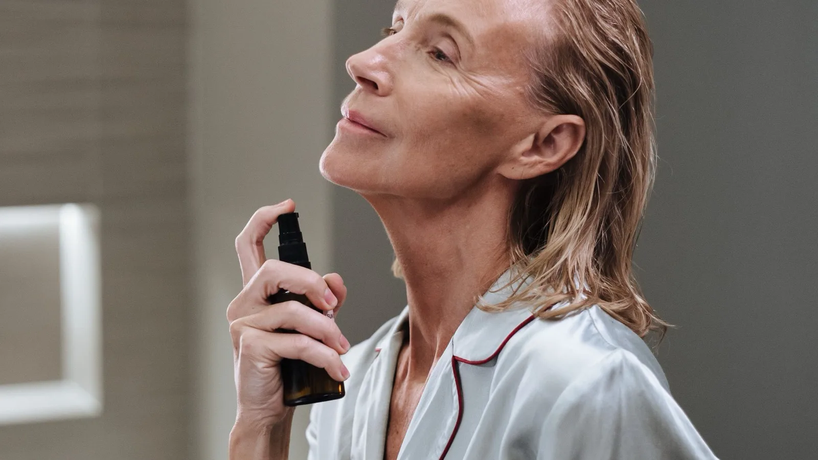 An elderly woman applying facial mist during a morning routine.