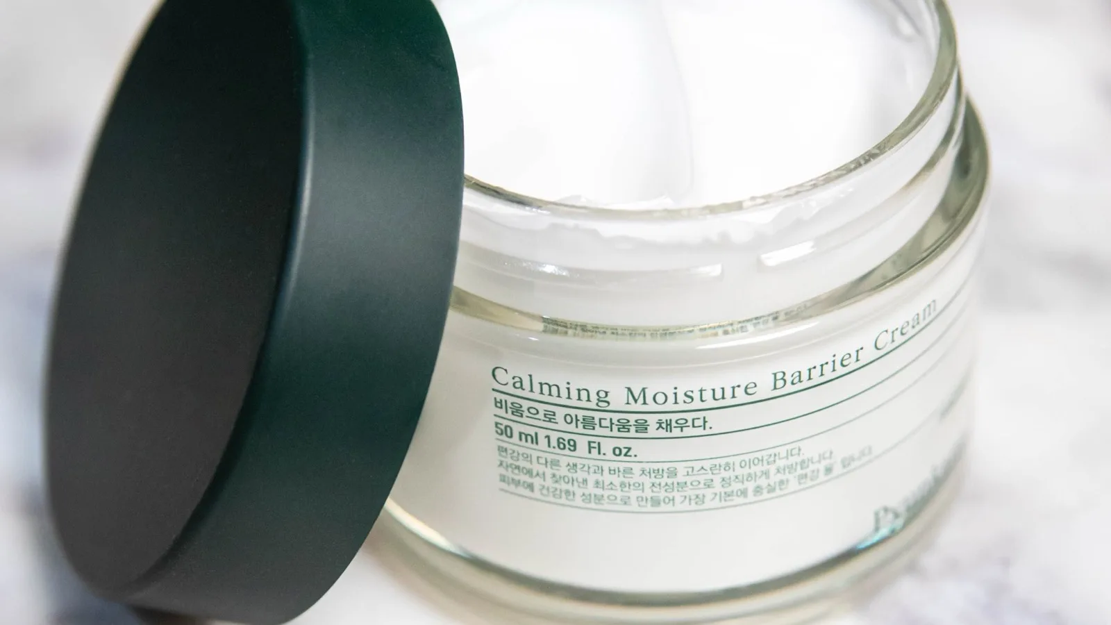 An open moisture barrier cream jar on a neutral surface.