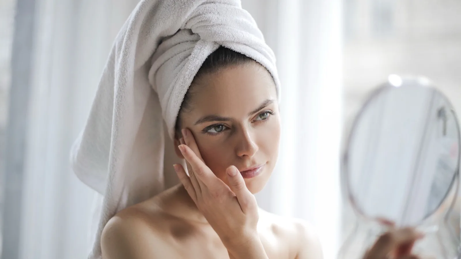 Woman checking her skin in a mirror while following a gentle skincare routine.