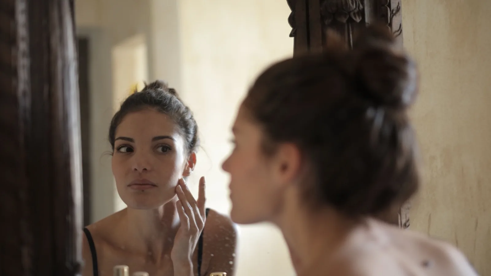 Woman checking her skin in a mirror while noticing a skincare concern.