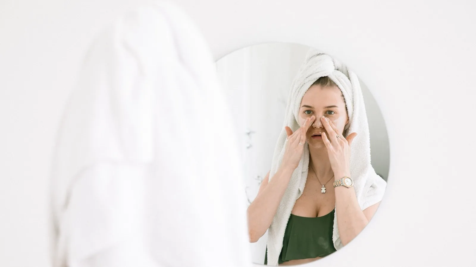 Woman performing a simple skincare routine in front of a bathroom mirror.