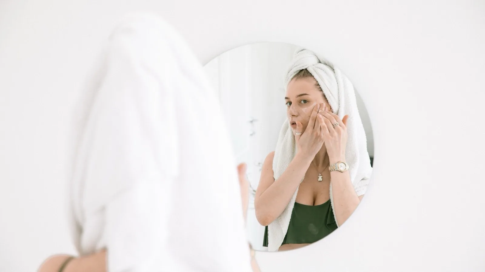 Woman applying face cream while looking in a bathroom mirror.