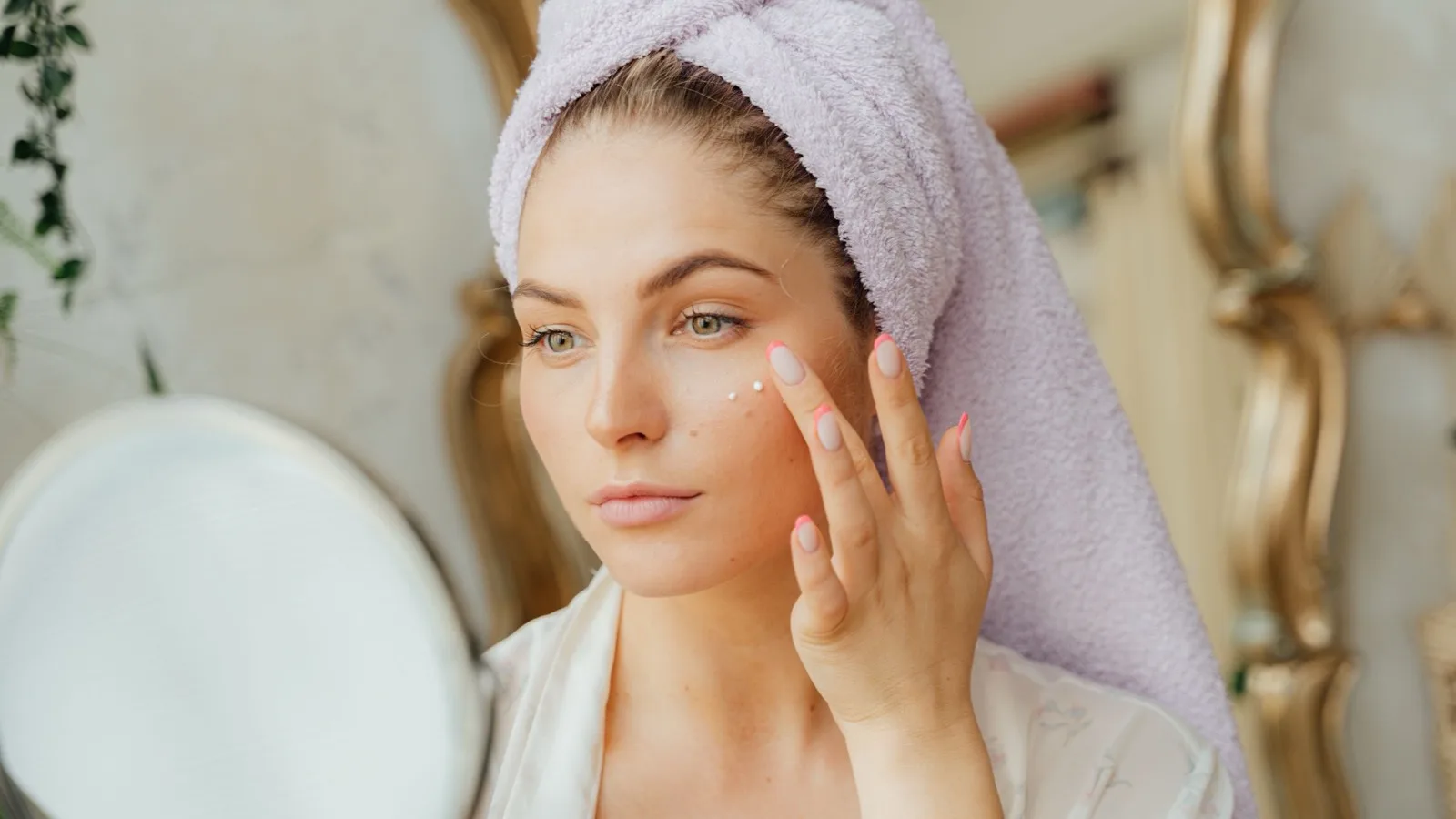 A woman applying moisturizer in front of a mirror.