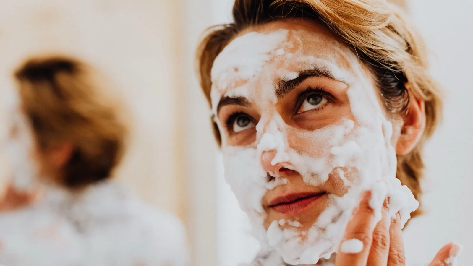 A person applying a gentle foaming cleanser to the face.