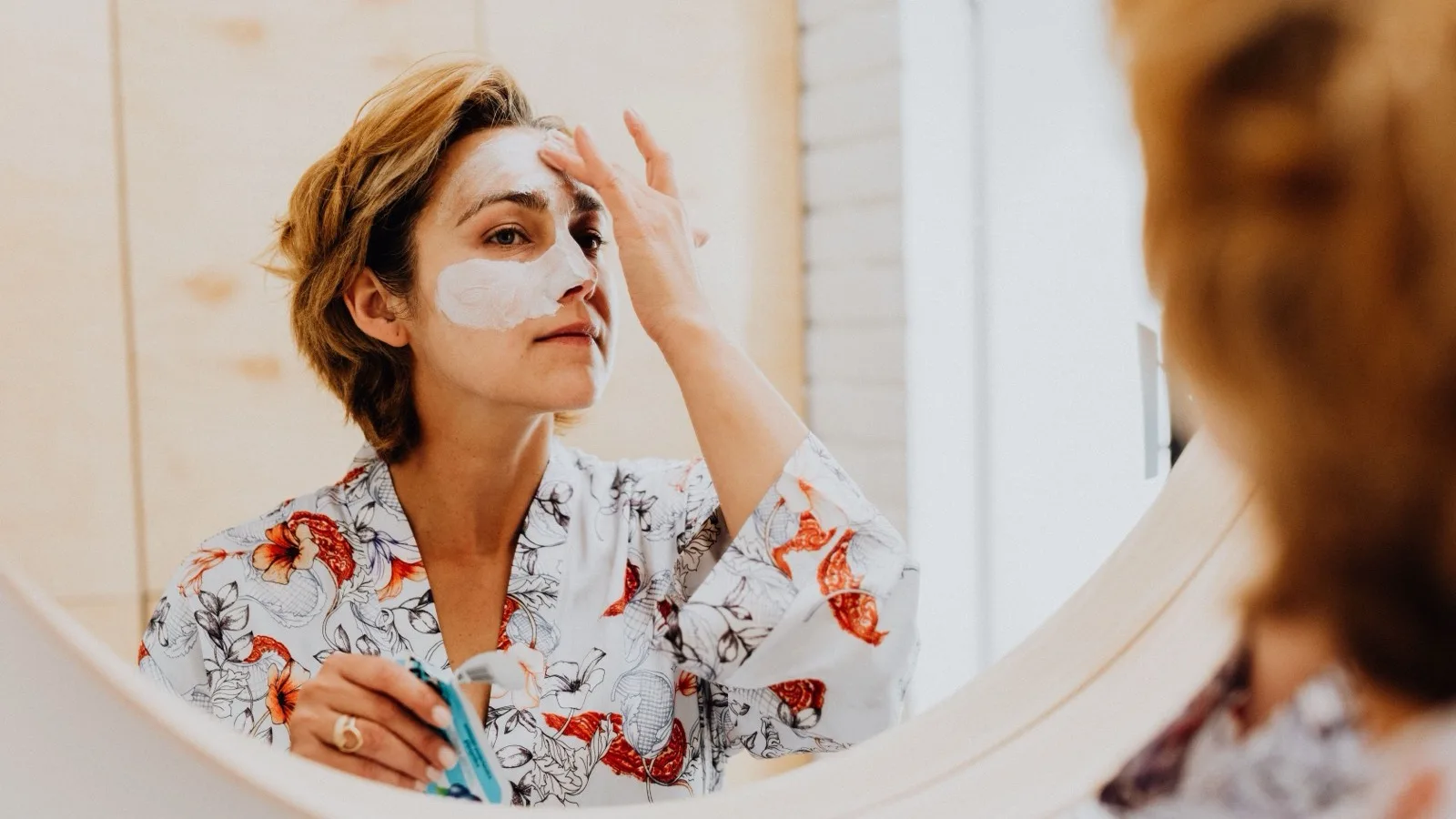A woman following a simple skincare routine in a bathroom mirror.