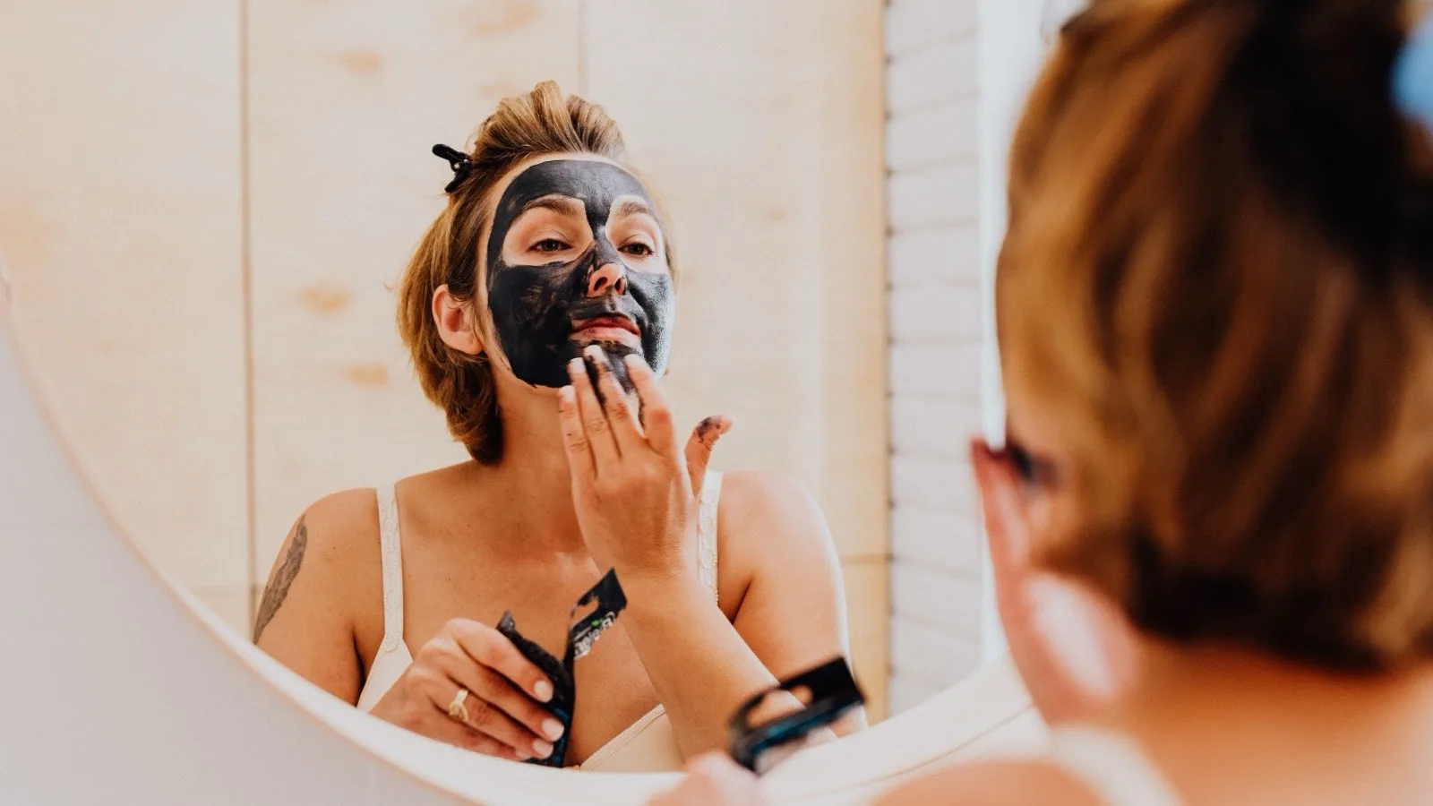 Woman applying a facial mask as one optional step in a skincare routine.