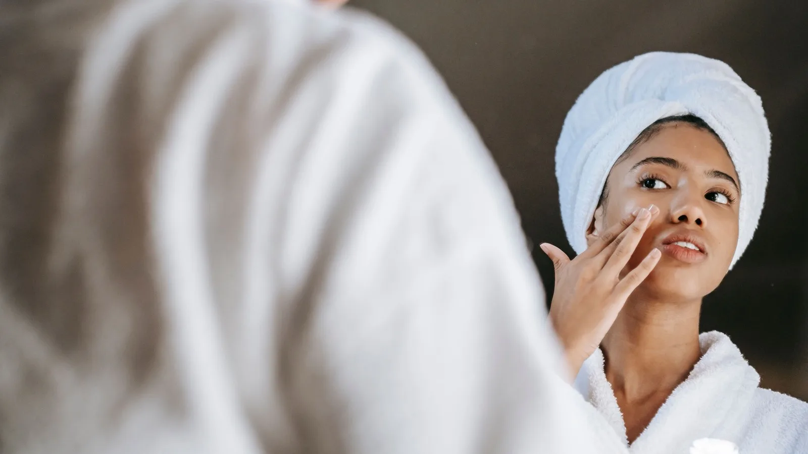 A woman applying cream while looking at her reflection.