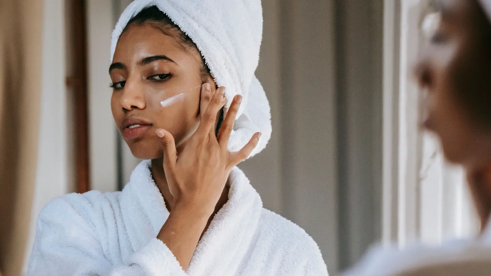 Woman applying moisturizer while getting ready for a morning skincare routine.