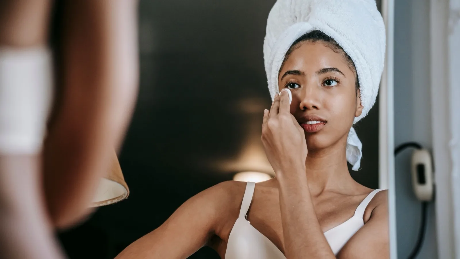 Woman gently cleansing her face while looking in a bathroom mirror.