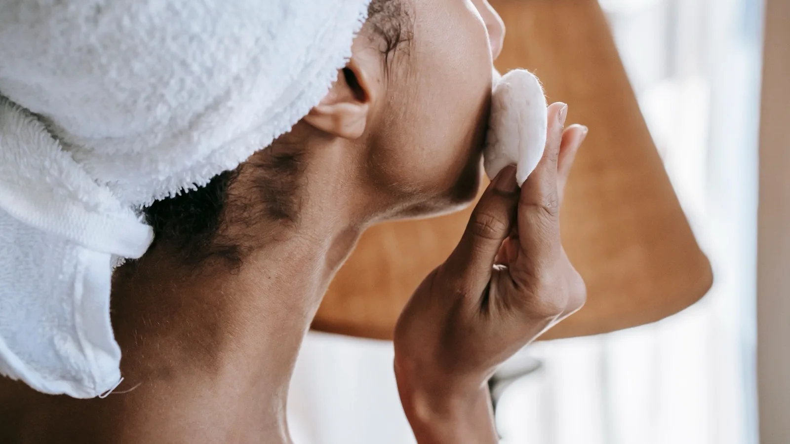 Woman gently cleansing her face with a cotton pad during a skincare routine.