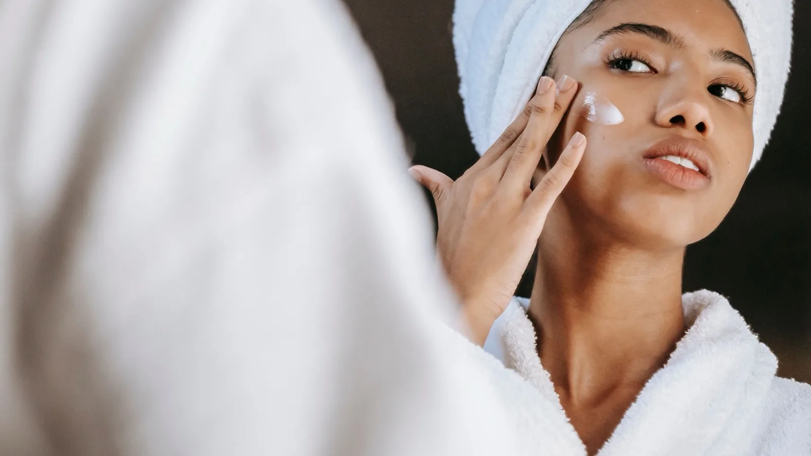 A person applying moisturizer during a skincare routine at home.