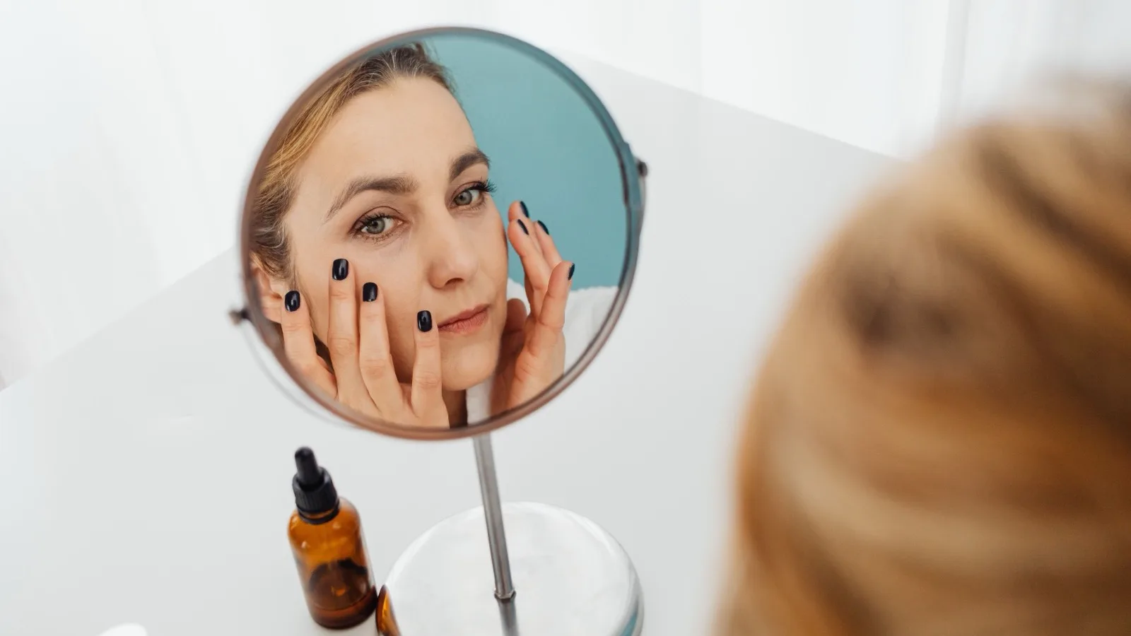 Woman considering her skincare routine while looking in a mirror.