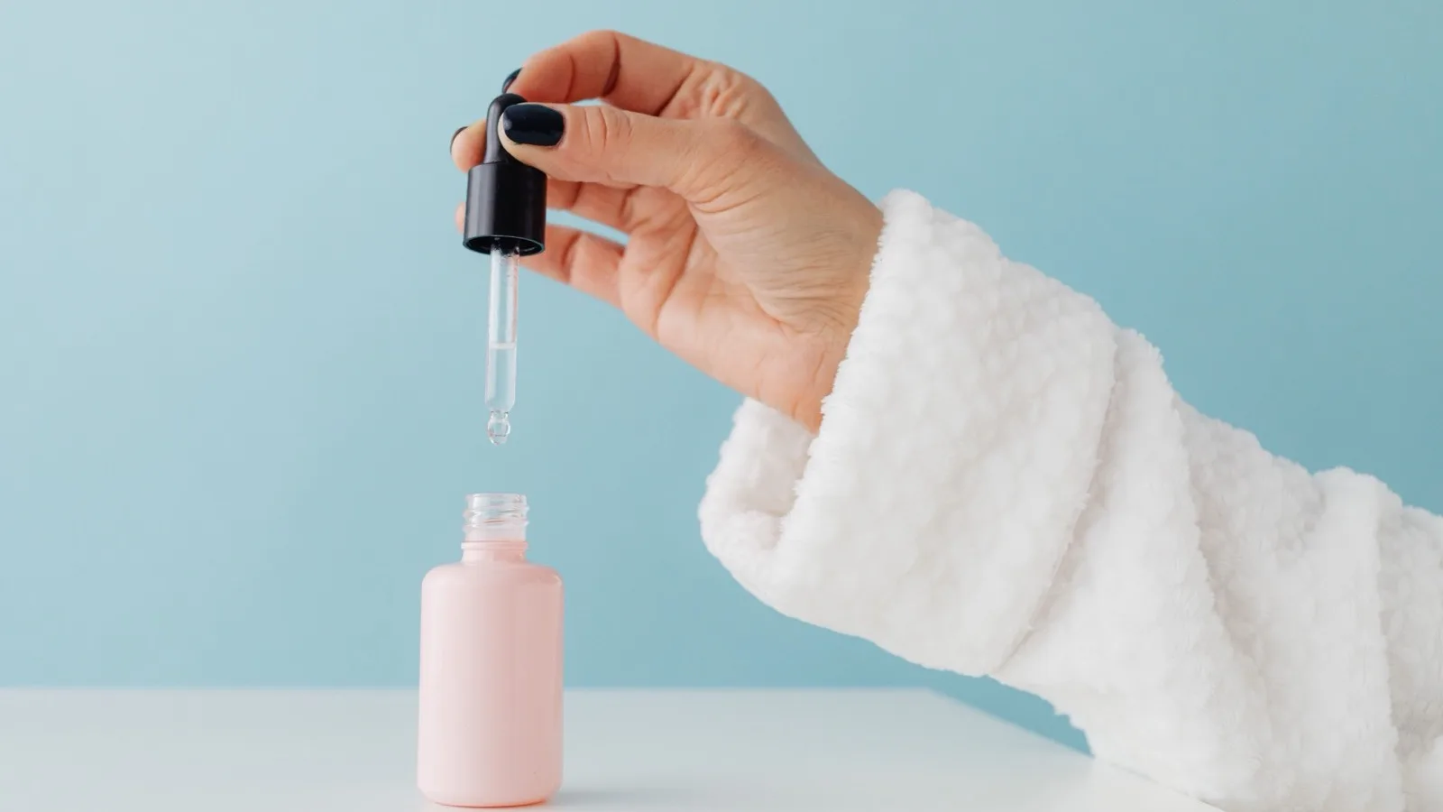 A hand applying a skincare serum with a dropper.