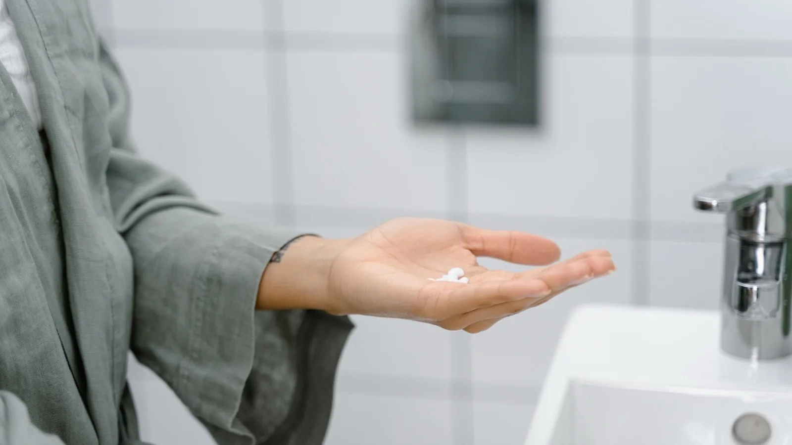 A hand holding moisturizer near a bathroom sink.