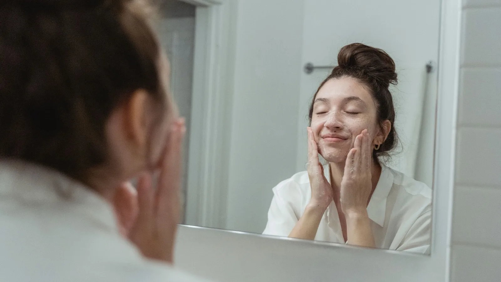 A person gently washing their face in a bathroom.