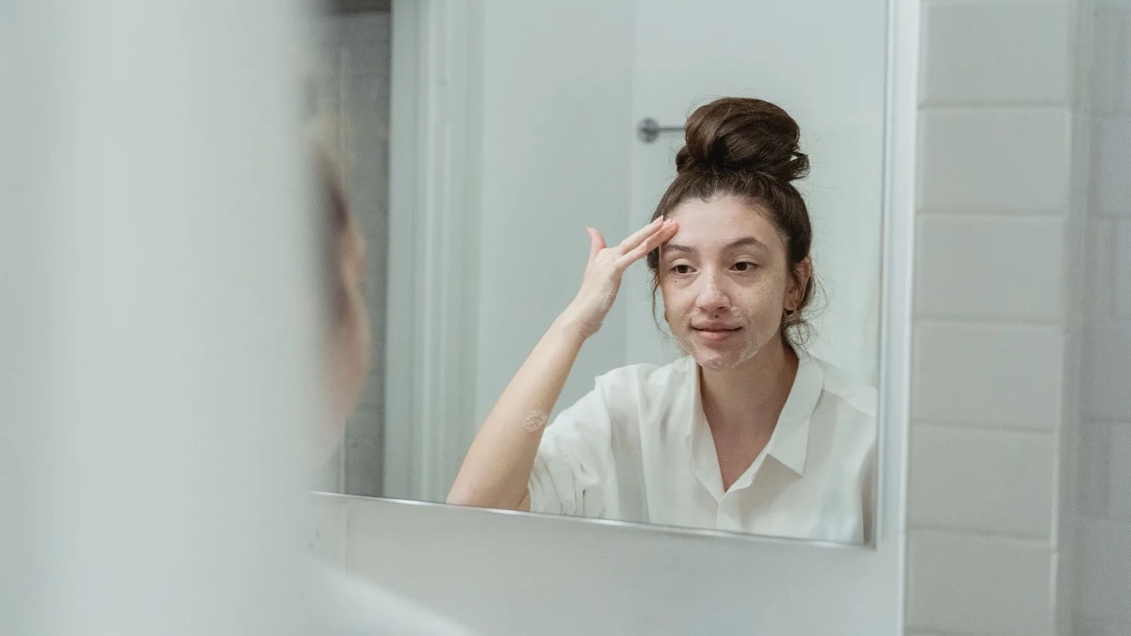 A woman applying facial cream in a bathroom.