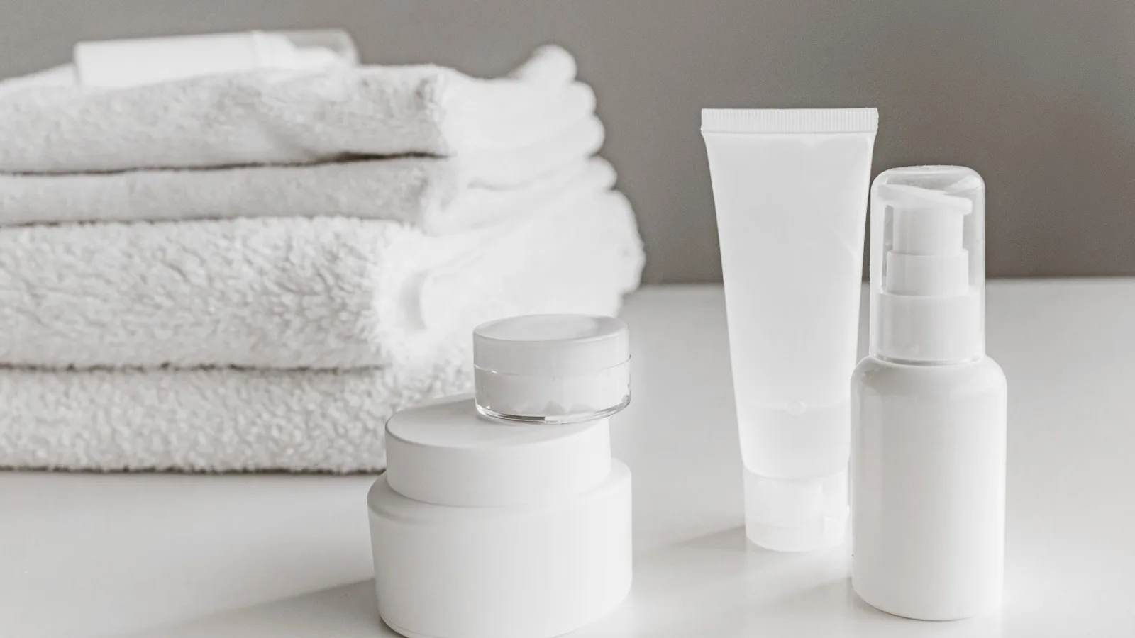 Minimal skincare products arranged with folded towels in a bathroom setting.