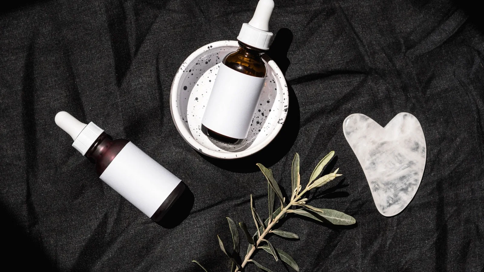 Unlabeled skincare bottles arranged on a dark neutral surface.