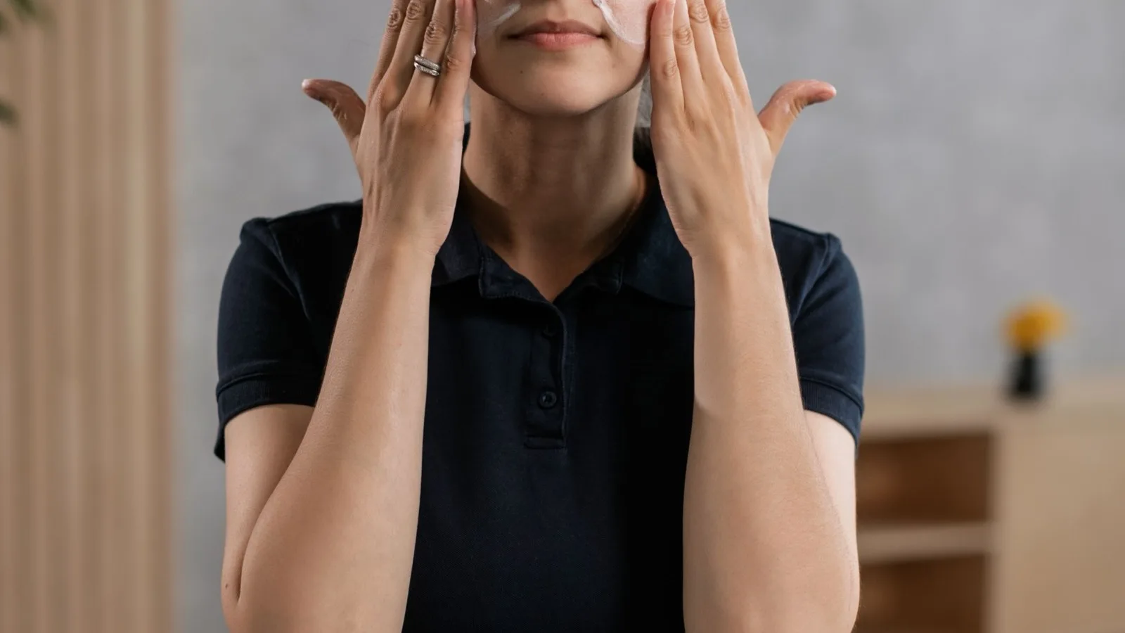 A woman applying facial moisturizer indoors as part of a skincare routine.