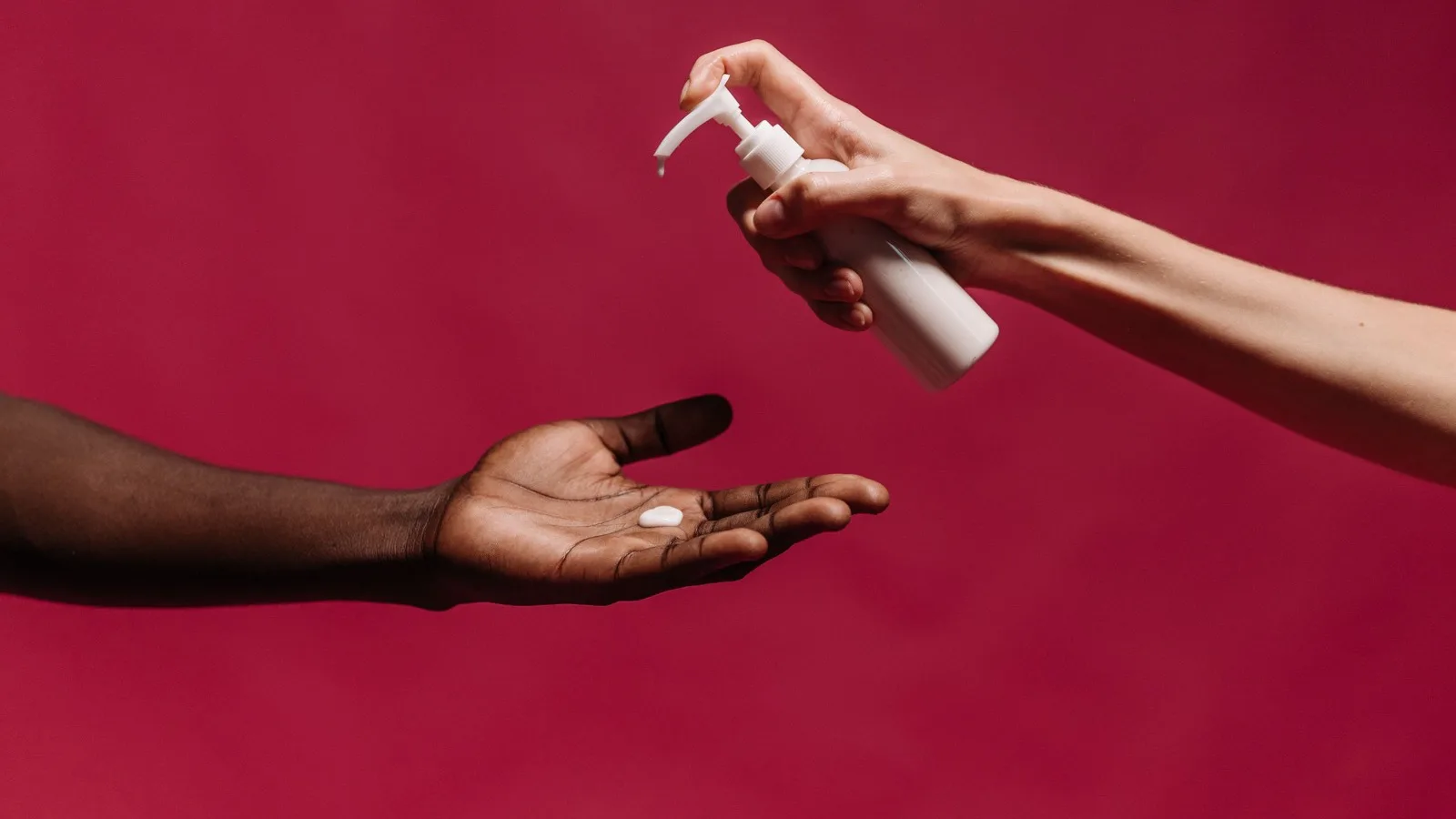 Hands dispensing a small amount of skincare lotion.