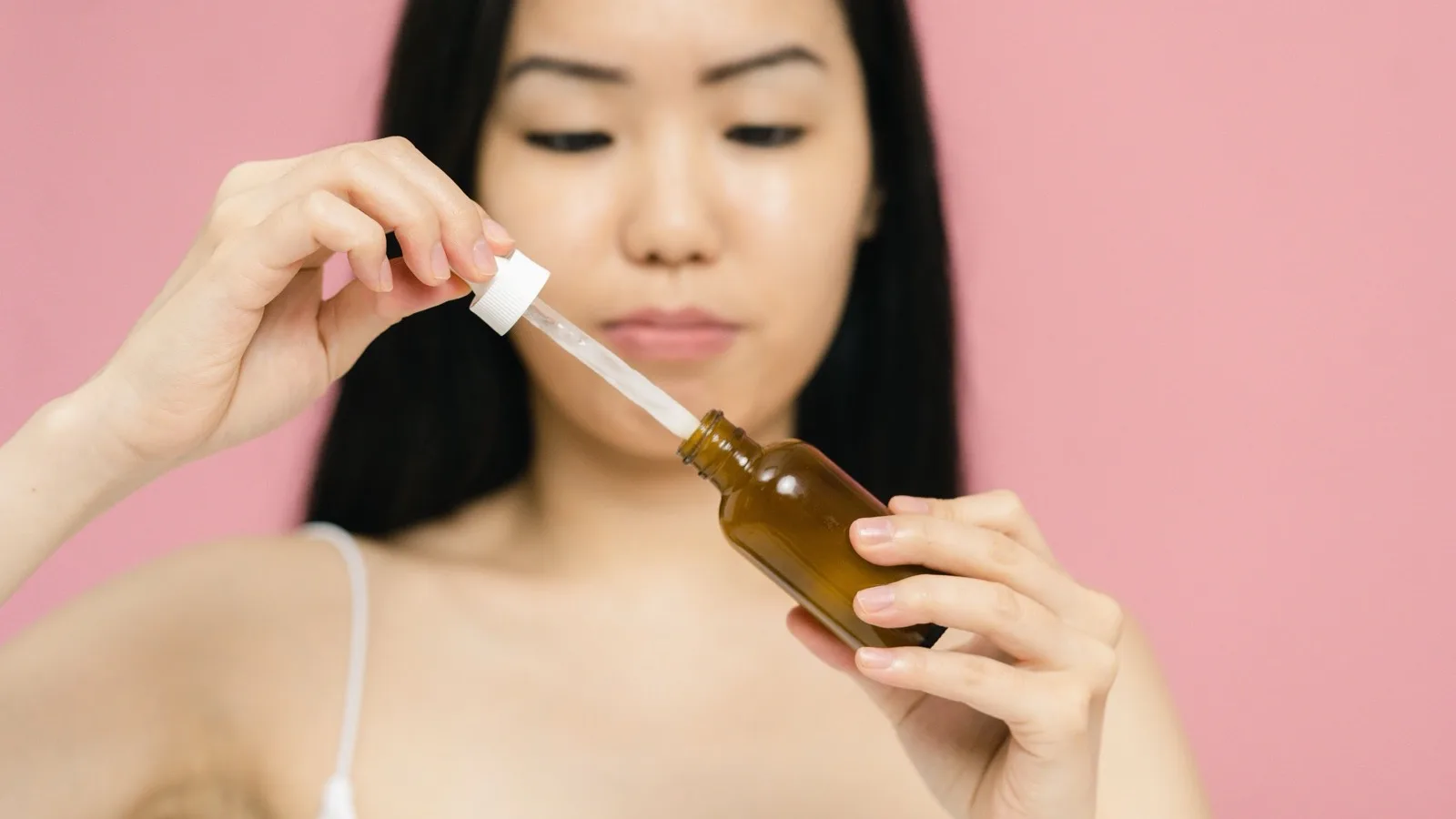 A woman holding a skincare serum bottle while considering her routine.