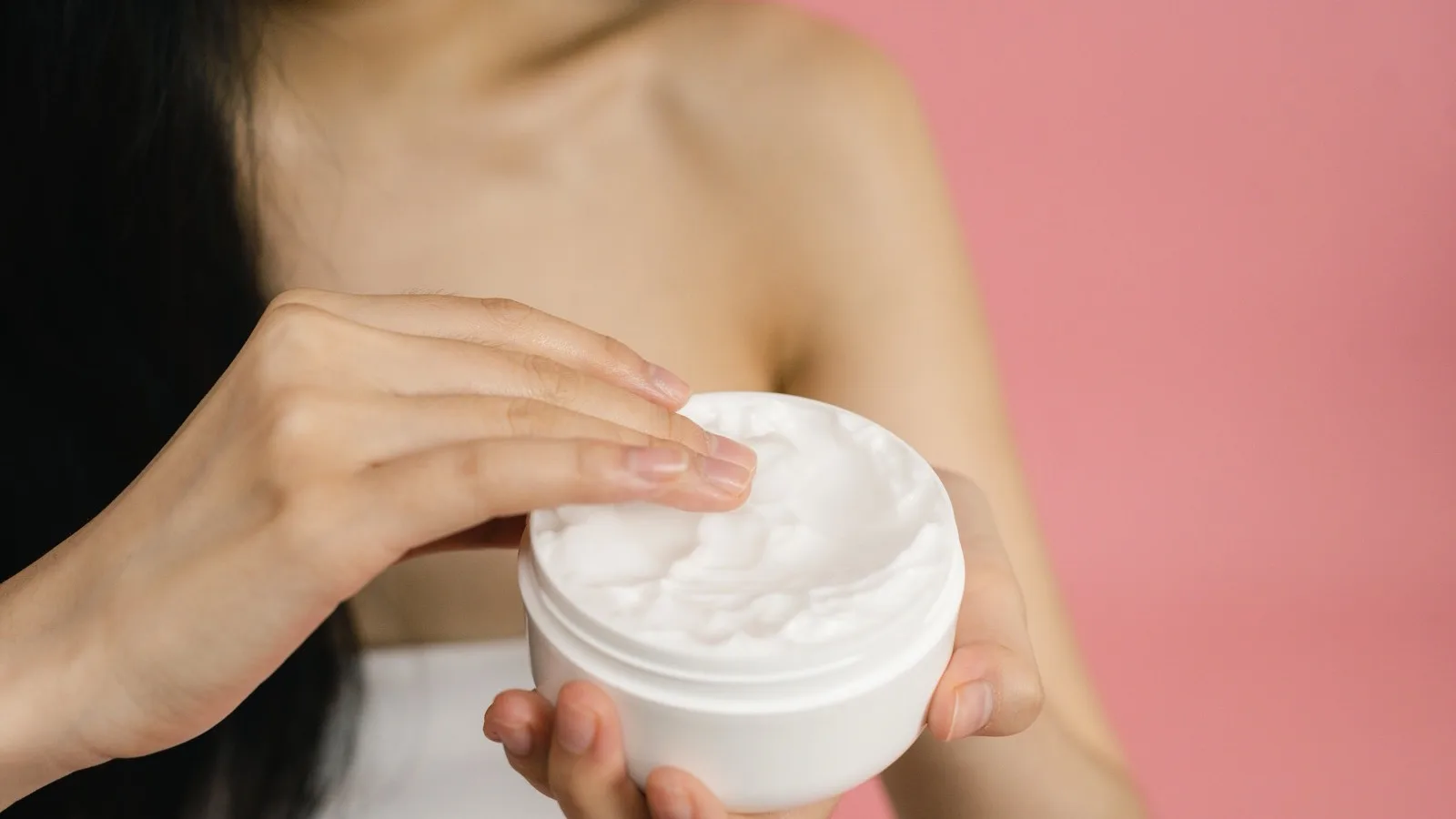 A woman applying cream from a jar as part of a skincare routine.