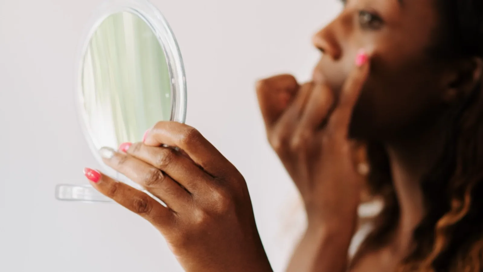 A woman checking her skincare routine with a handheld mirror.