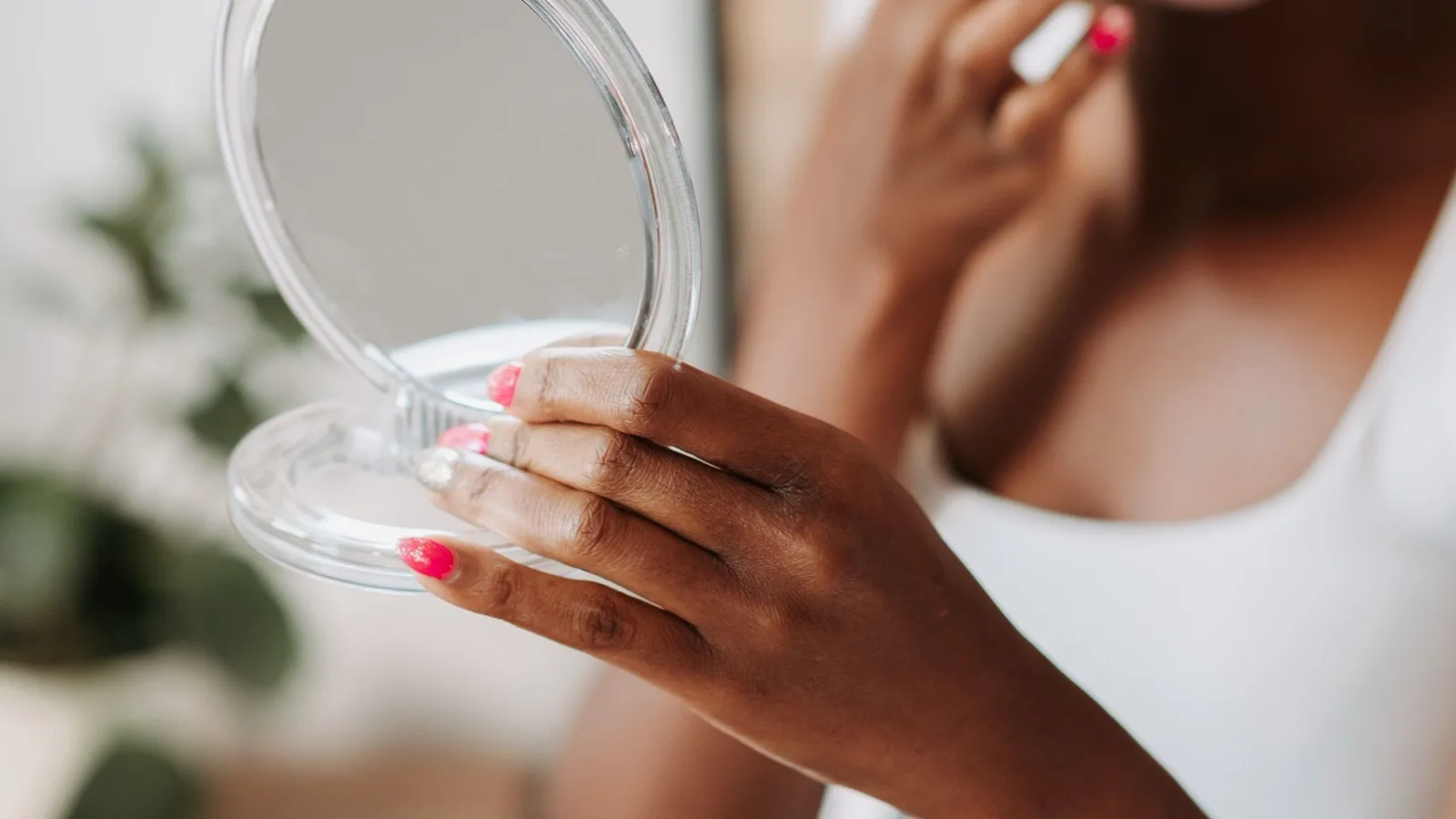 A woman using a handheld mirror during a personal skincare routine.